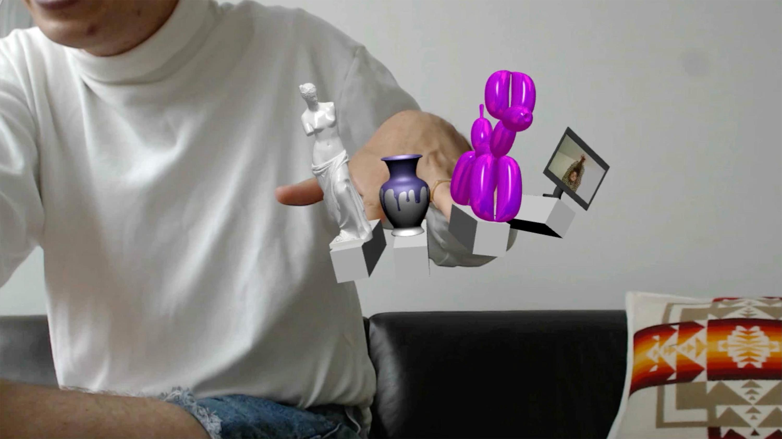 A person extends their hand toward you. Superimposed on their fingertips are digitally rendered images of a vase, sculpture, balloon dog, and screen.